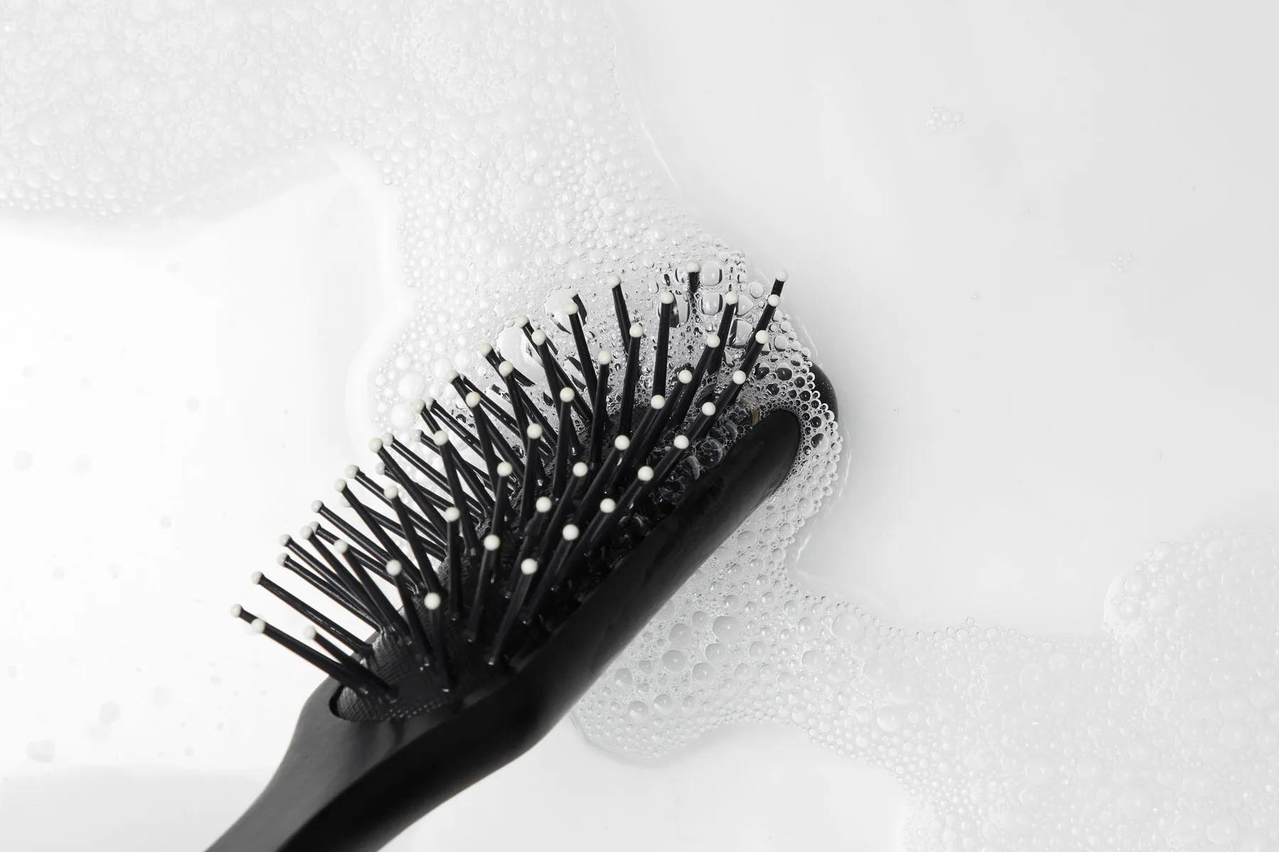 a hairbrush getting clean in water with a cleansing or clarifying shampoo